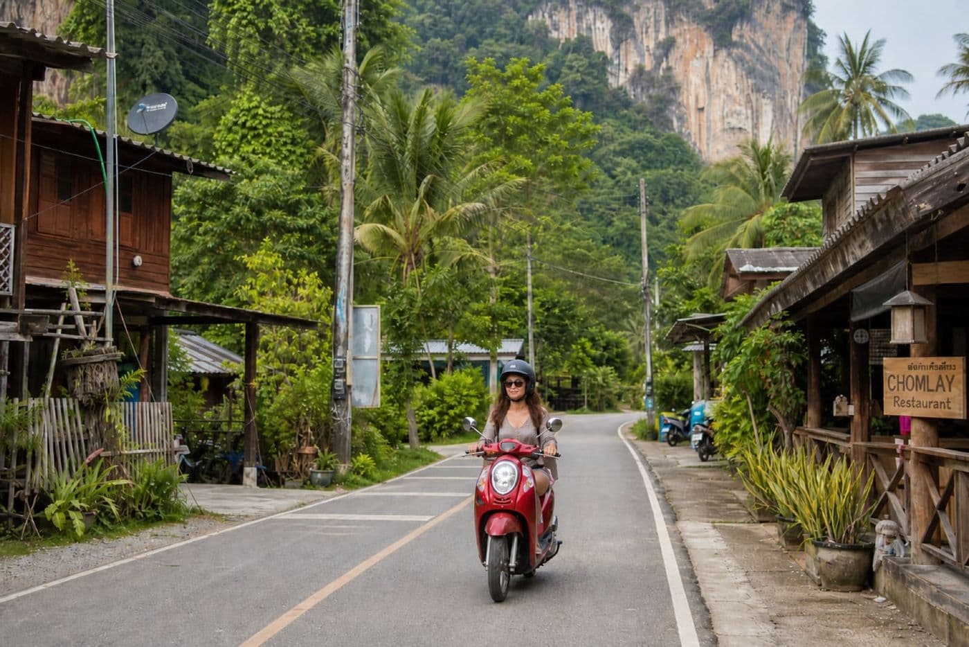 Tourist wearing a helmet while riding a scooter through a quiet local Thai village near Krabi