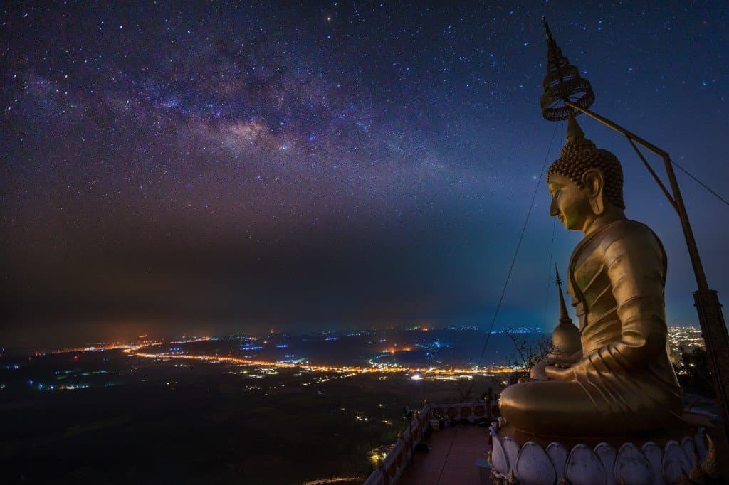 Golden Buddha at the summit of Tiger Cave Temple at night with Milky Way and Krabi city lights below