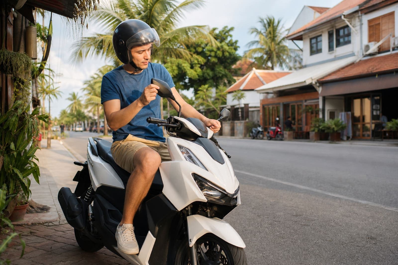 Beginner scooter rider adjusting mirrors before riding in Thailand